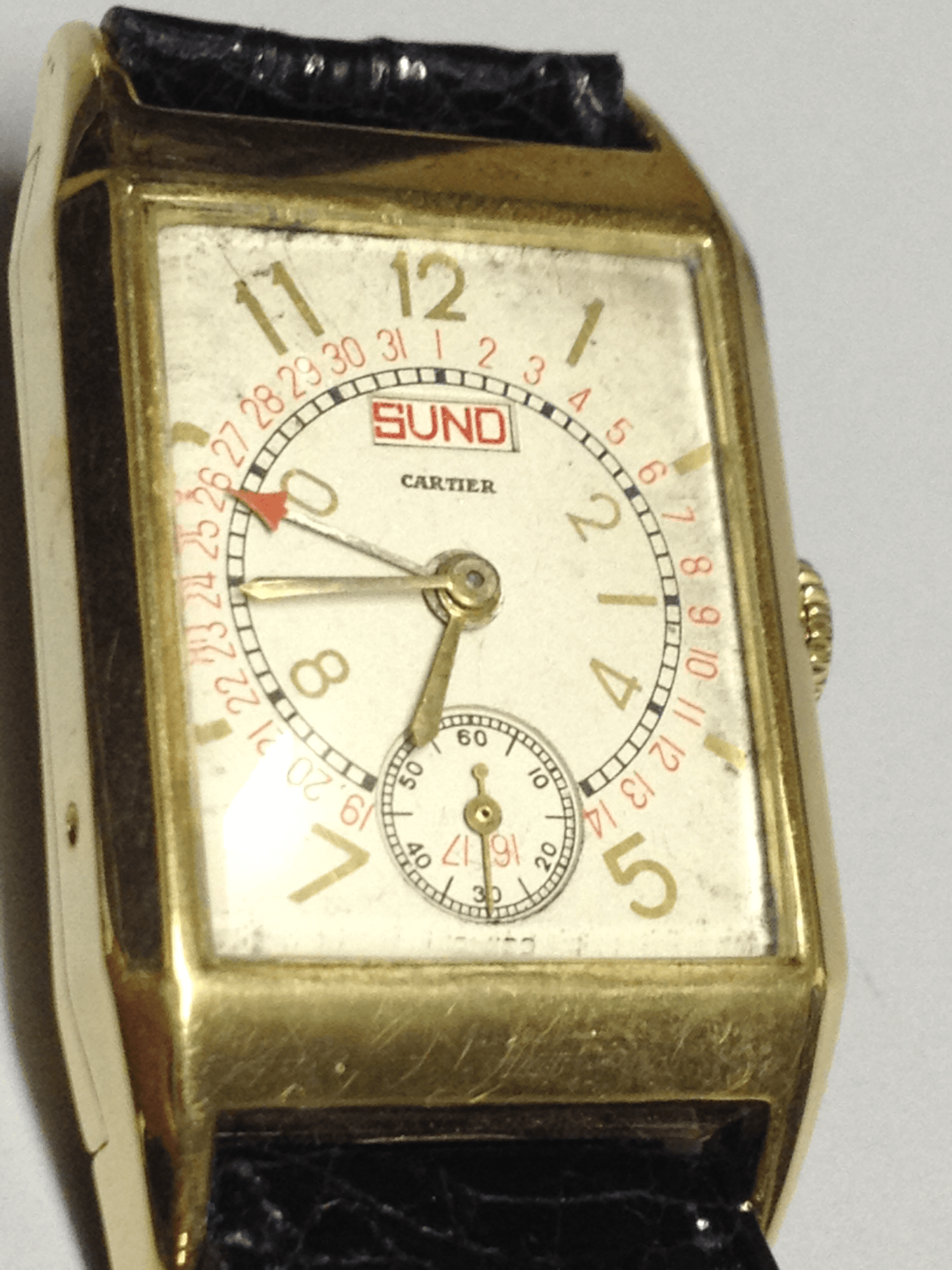 Rare 1960 Cartier Tank Day Date in yellow gold, featuring a multi-layered dial with Arabic numerals, day and date display, and a manual-winding movement.