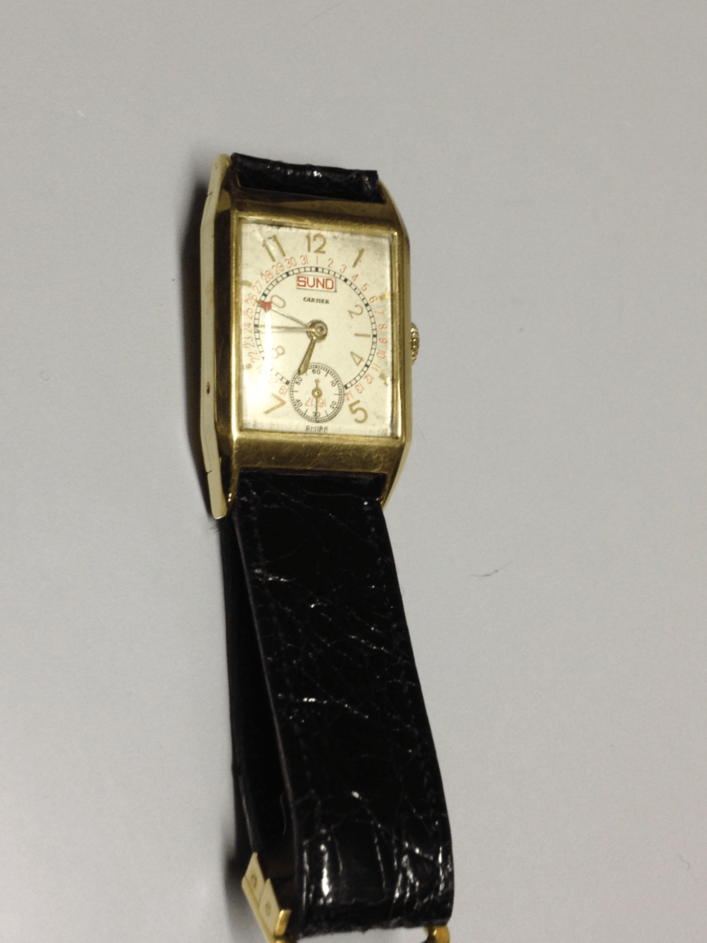 Rare 1960 Cartier Tank Day Date in yellow gold, featuring a multi-layered dial with Arabic numerals, day and date display, and a manual-winding movement.