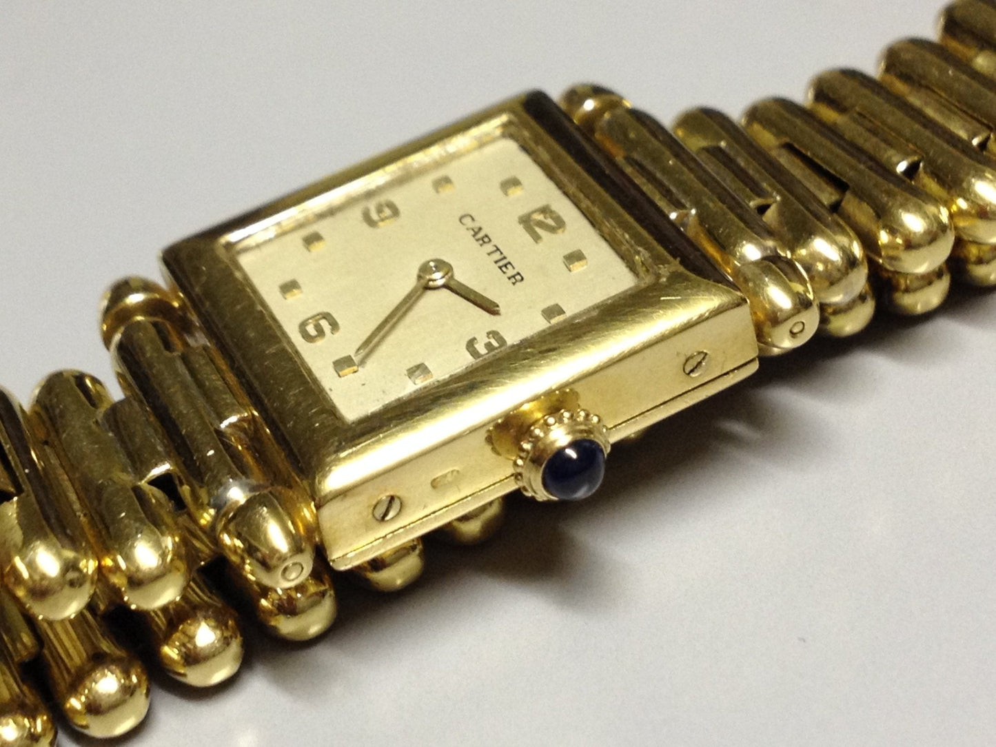 Vintage Cartier Square Watch in yellow gold, circa 1950, featuring a champagne dial, Arabic numerals, cabochon sapphire crown, and bullet-link bracelet.
