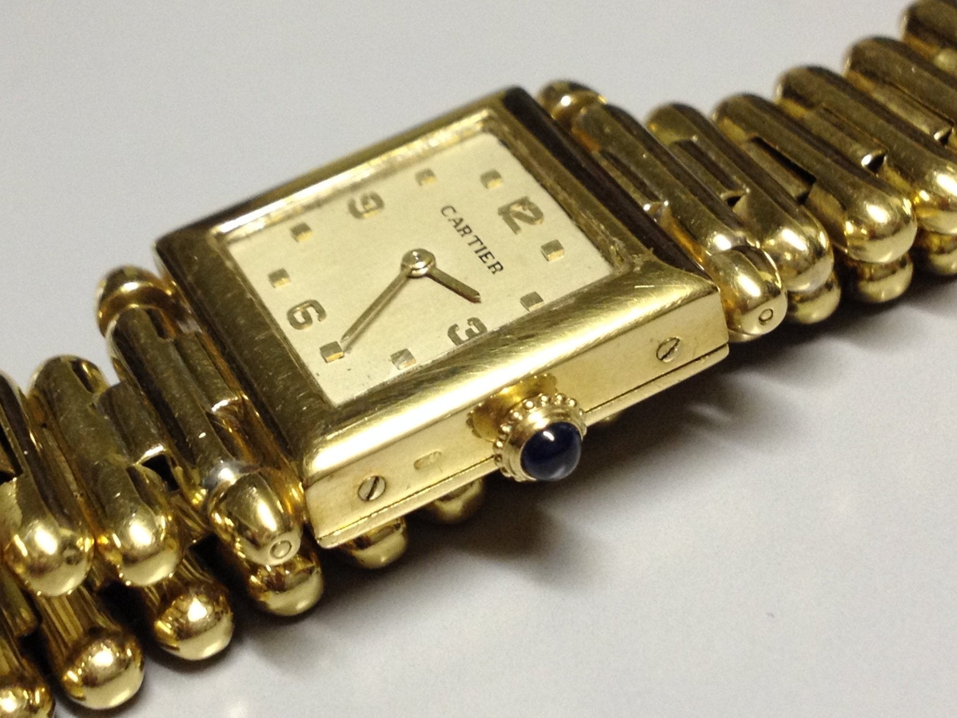 Vintage Cartier Square Watch in yellow gold, circa 1950, featuring a champagne dial, Arabic numerals, cabochon sapphire crown, and bullet-link bracelet.