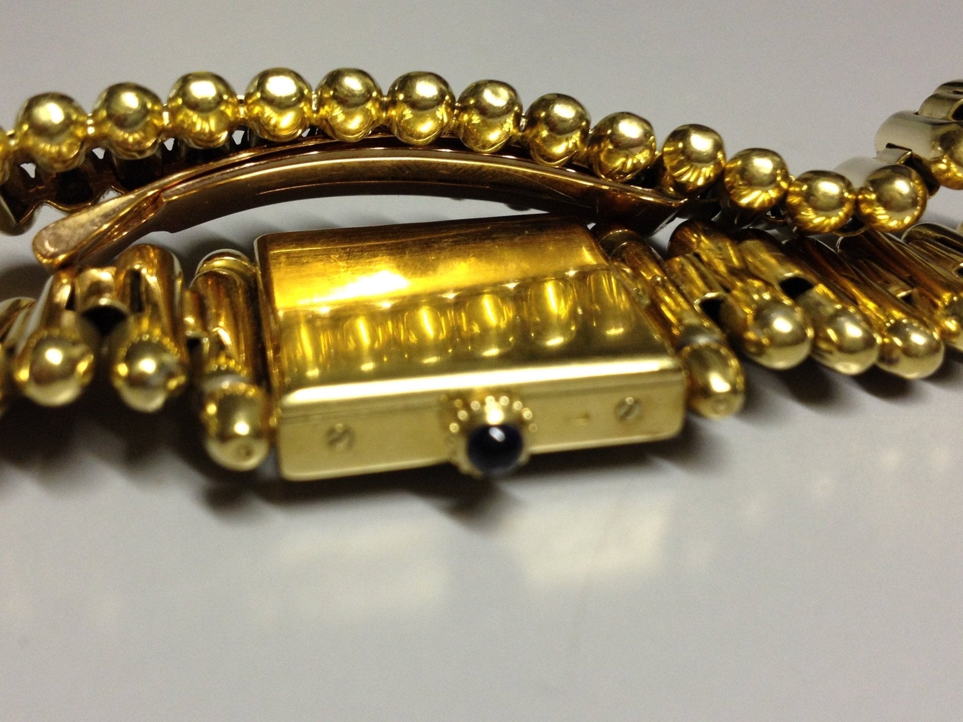 Vintage Cartier Square Watch in yellow gold, circa 1950, featuring a champagne dial, Arabic numerals, cabochon sapphire crown, and bullet-link bracelet.